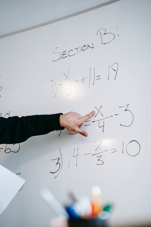 A hand pointing at an equation written on a white board